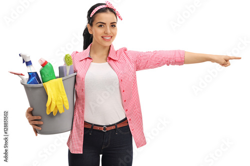 Happy woman holding a bucket filled with cleaning products and pointing right