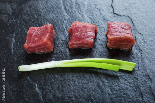 Three cubes of meat and green onions on the black table