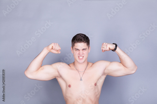 young man with relief muscles in jeans with a naked torso on a gray background