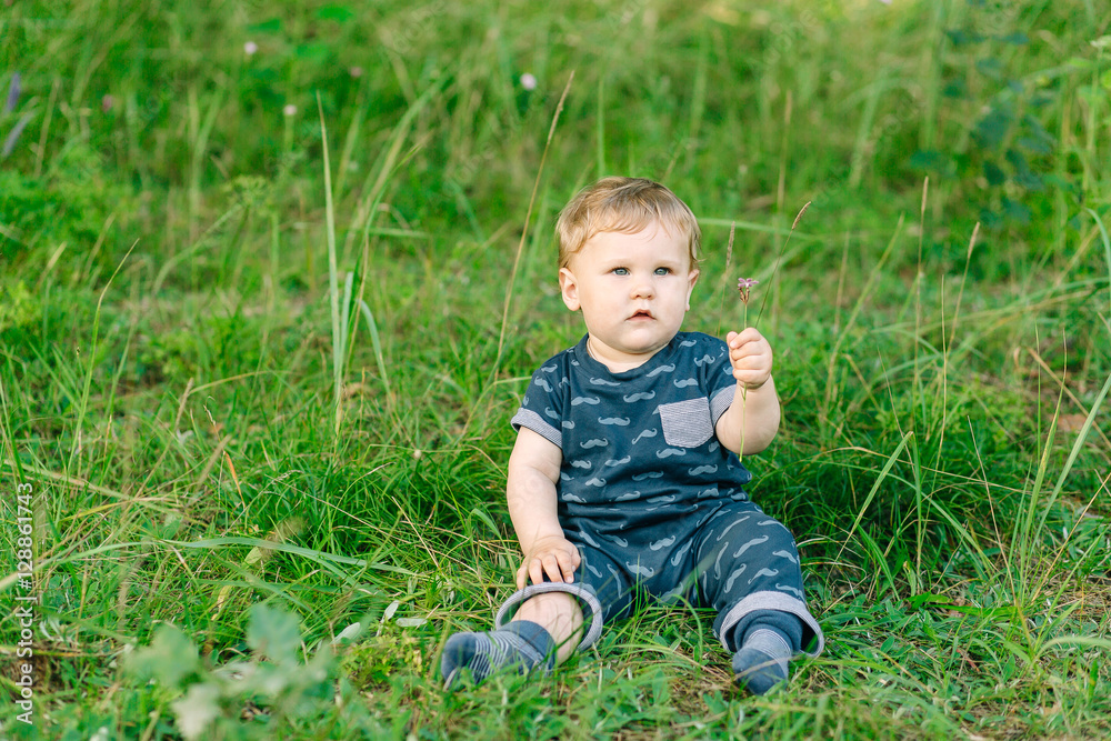 chubby little boy in dark clothes sitting on the grass in the park on a summer day