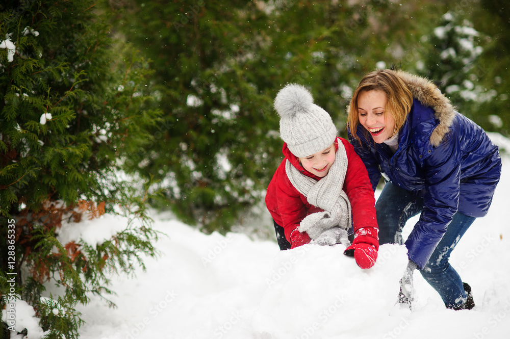 Obraz premium Young woman and girl of school age build a snowman.