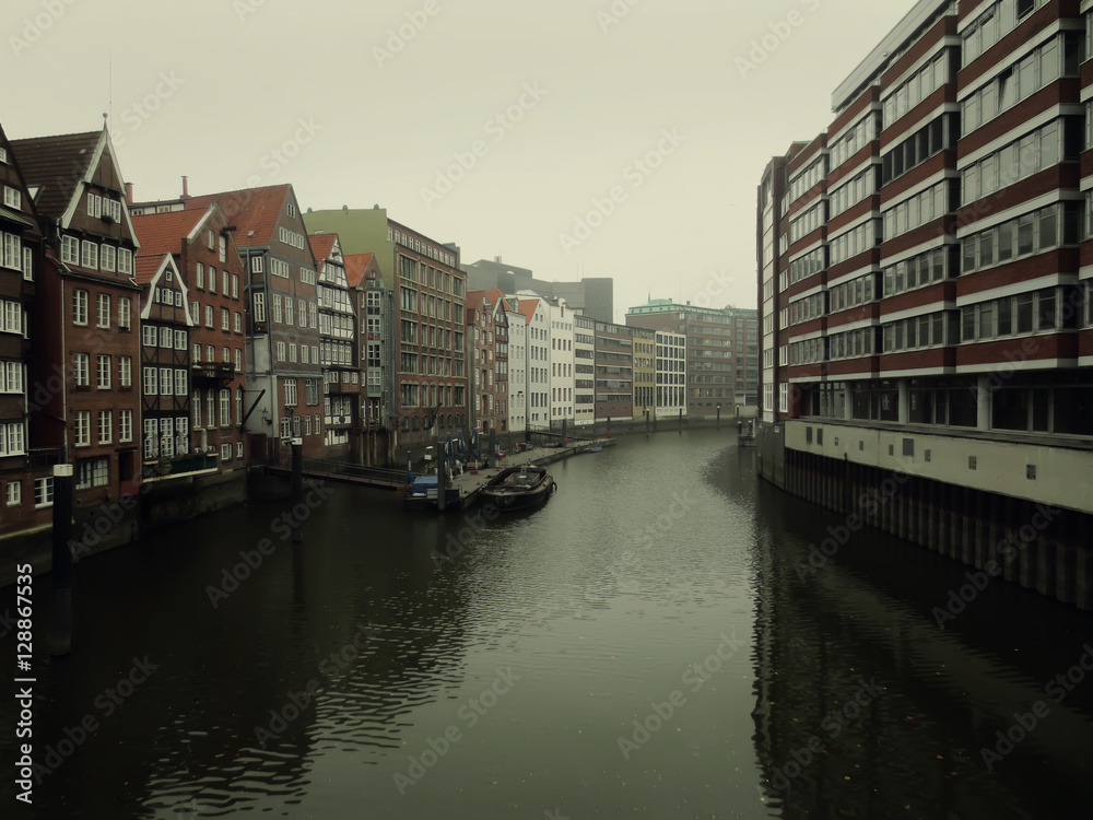 City landscape of river running between houses in Hamburg, Germany in rainy weather. Photo in low key.