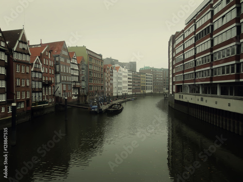 City landscape of river running between houses in Hamburg  Germany in rainy weather. Photo in low key.