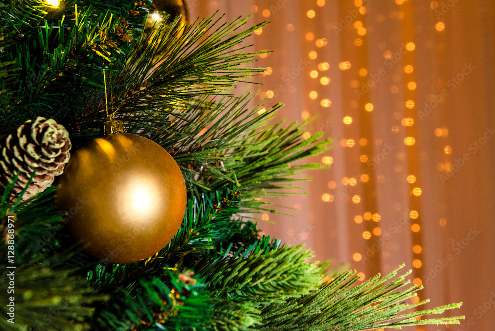 A close picture of a bright golden christmas toy hanging on a green tree, blurred warm background with golden tinsel. Decorated Christmas tree on lights background, copyspace.
