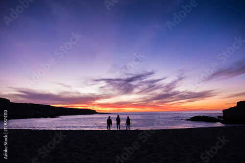 Silhoette of three freinds standing on the sandy beach at sunrise