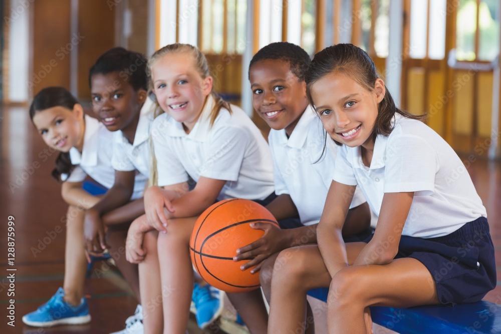 Naklejka premium Portrait of school kids sitting in basketball court