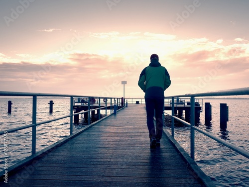 Tall man stand on mole wooden board and looking over ocean to Sun. Empty wharf 