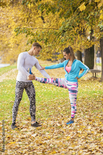 Beautiful young couple stretching together and preparing for run in the park. Autumn environment.