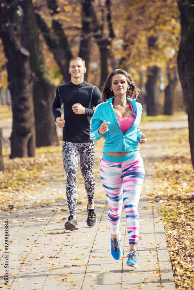 Beautiful young couple running together in the park. Autumn environment. Beautiful young couple running together in the park. Autumn environment.