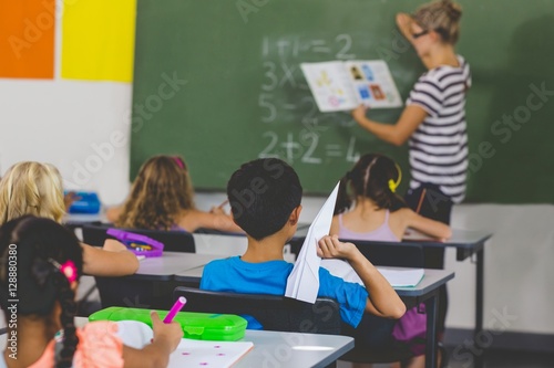 Boy with a paper plane while teacher teaching in classroom photo