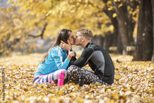 Beautiful young couple resting and kissing after successful training in the park. Autumn environment.