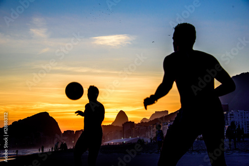 Beautiful sunset and silhouettes of men playing dar toques na bola game at Copacabana beach, Rio de Janeiro, Brazil