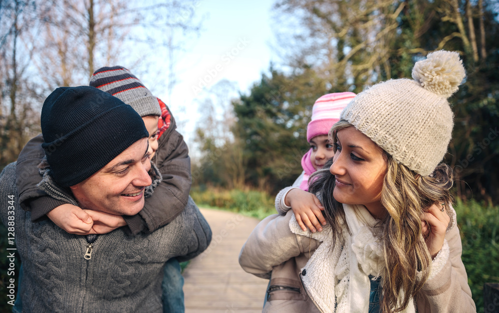 Portrait of smiling parents giving piggyback ride to happy children over a wooden pathway into the forest Portrait of smiling parents giving piggyback ride to happy children over a wooden pathway into the forest