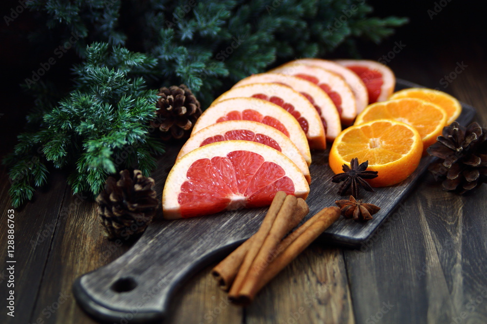 грейпфрут и мандарины на разделочной доске с еловой веткой и шишками ...