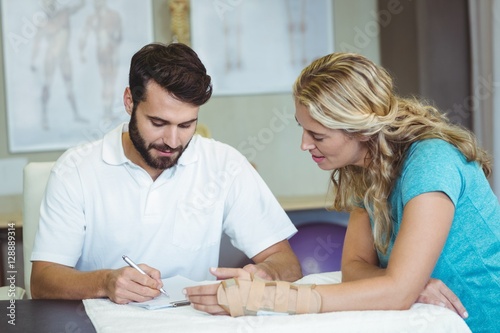 Foto Physiotherapist writing report next to the patient