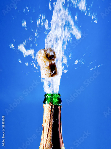 Fotografie Bottle of champagne with a popping cork (against a bright blue background)