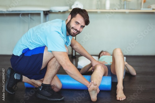 Physiotherapist doing leg therapy to a woman using foam roll