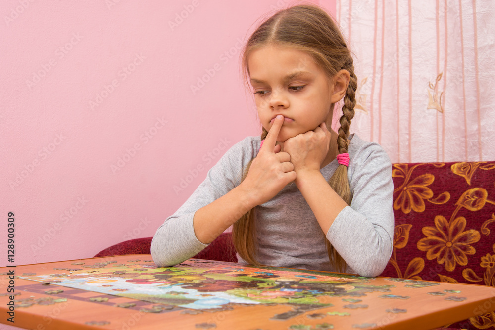 The child is thinking how to assemble a picture from puzzles The child is thinking how to assemble a picture from puzzles
