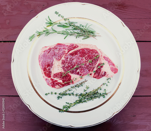 Raw rib-eye steak on plate, wooden table, toned