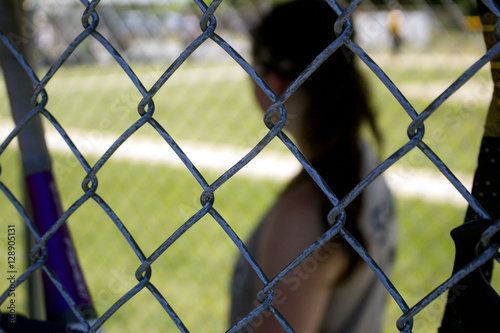 Through fence, girl in dugout waiting for her turn at bat