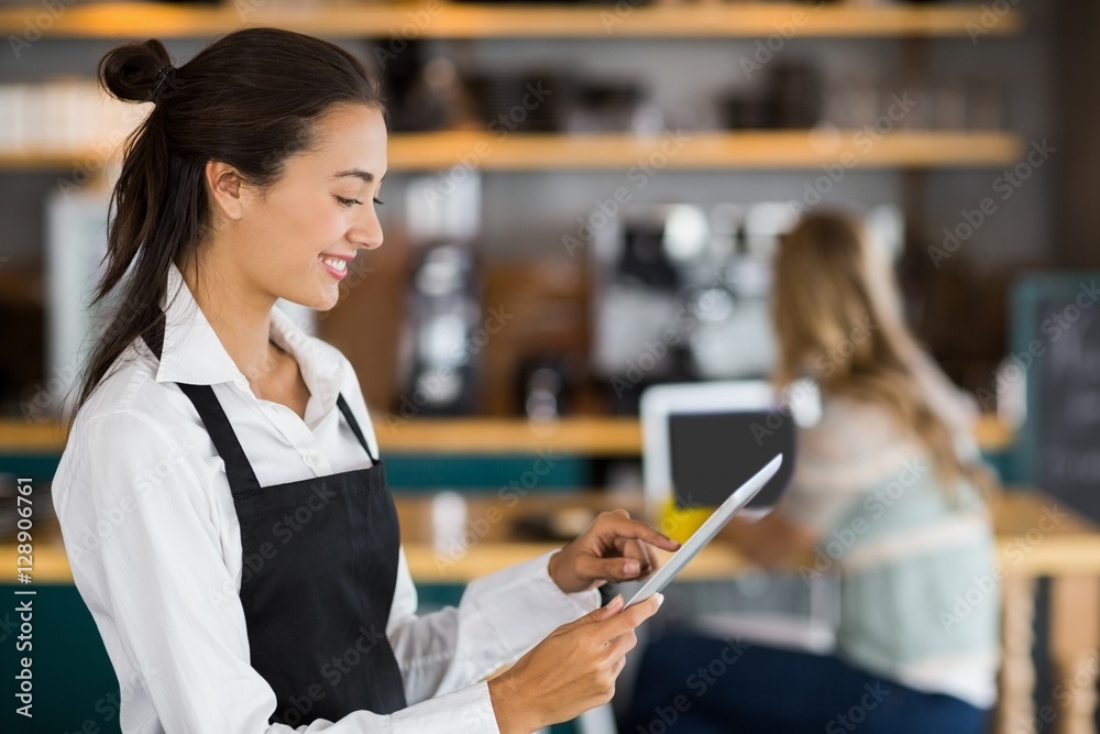 Obraz premium Smiling waitress using digital tablet