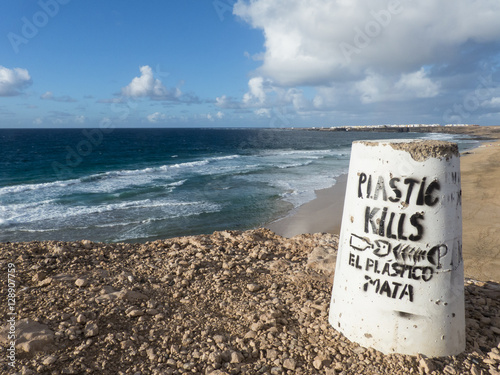 Signpost at the beach reading plastic kills in english and Spani