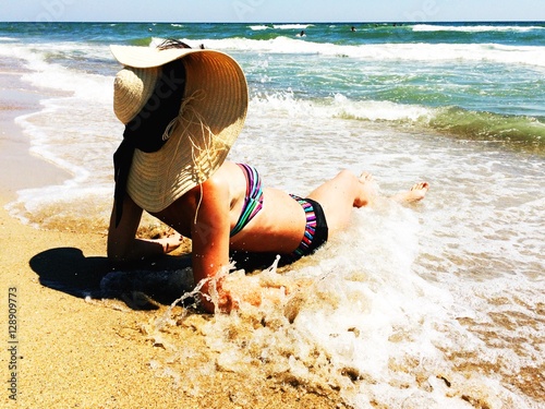 Woman at the seashore in straw hat in sea waves photo