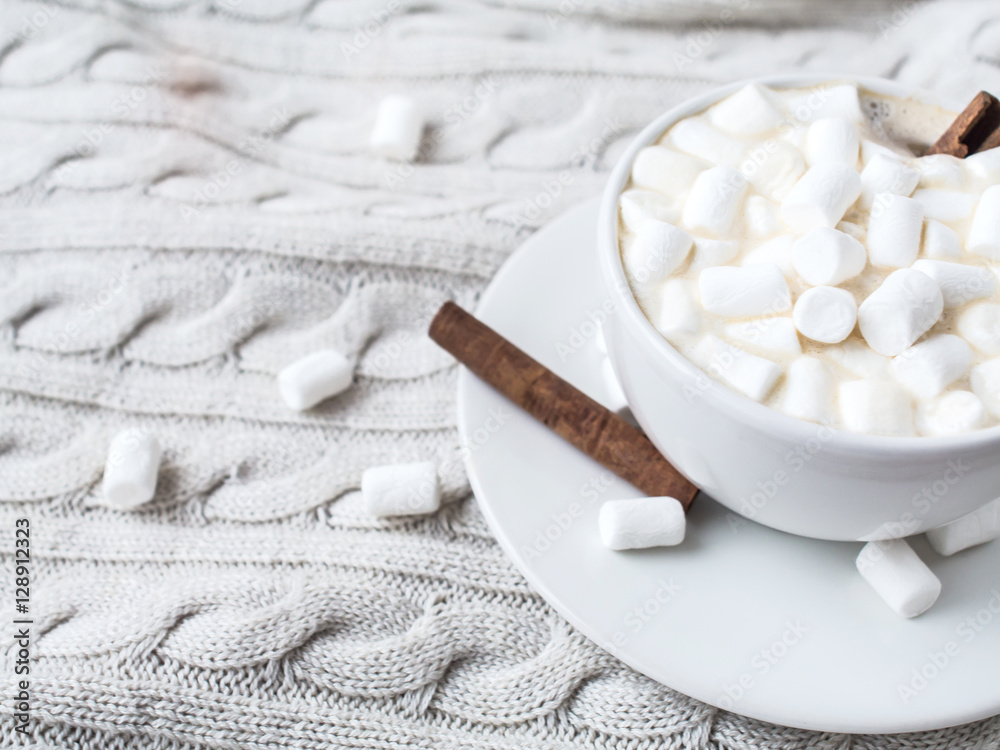 A cup of hot cocoa with Marshmallow and cinnamon sticks on a knitted beige background of Christmas decorations and mandarins, cones. Shallow Selective focus. Copyspace.