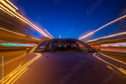 The car moves at great speed at the night. Blured road with lights with car on high speed. The view from the front to back.