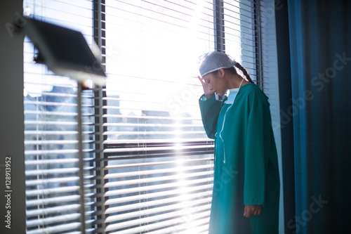 Tensed female surgeon standing near window in hospital photo