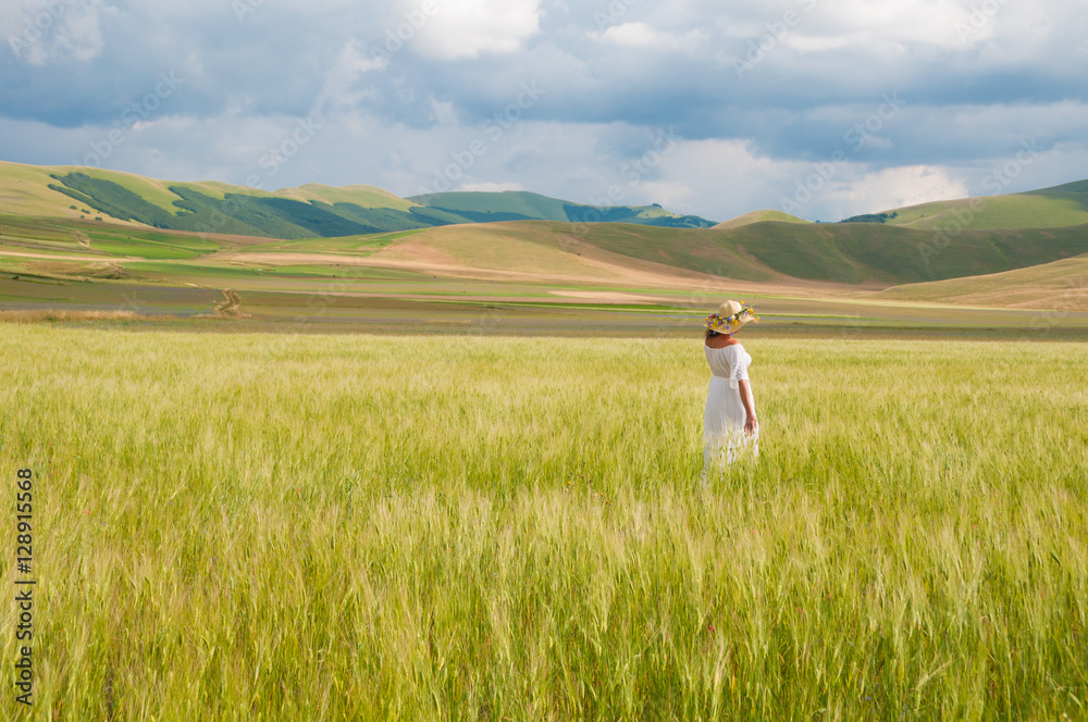 Girl in White dress and straw hat walking among fields in countryside