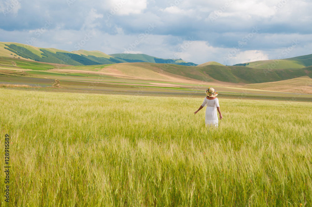 Girl in White dress and straw hat walking among fields in countryside Girl in White dress and straw hat walking among fields in countryside