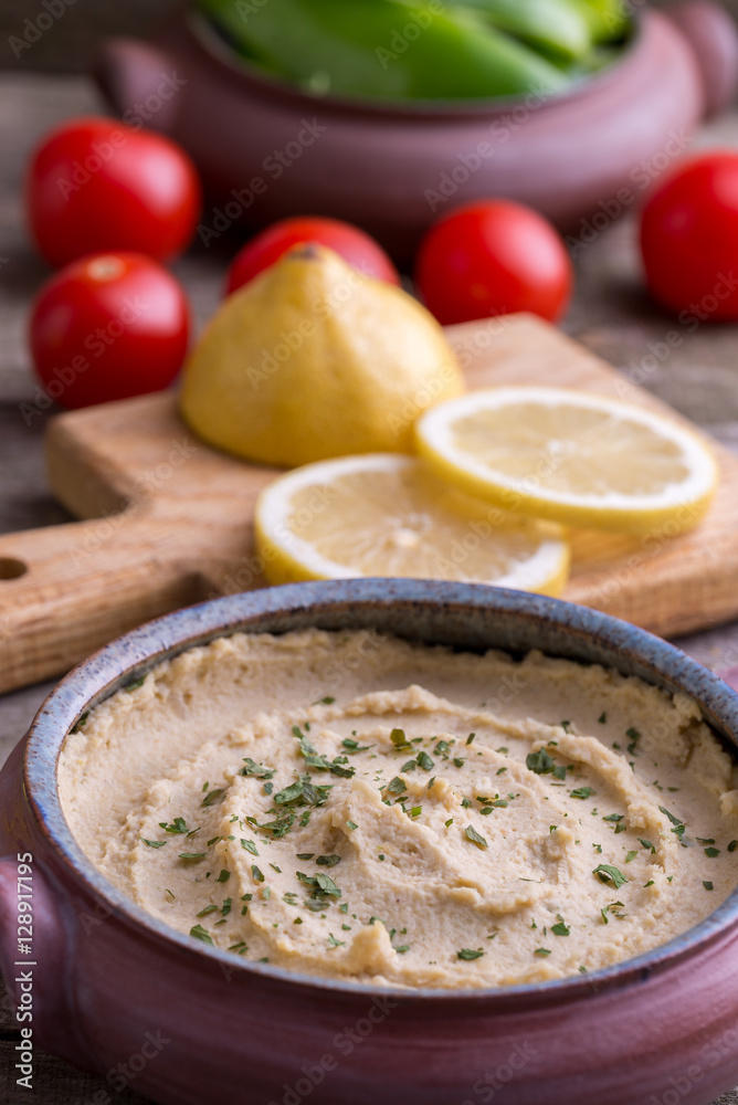 Humus in homemade bowl with vegetable around.