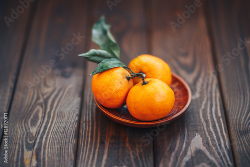 tangerines on wooden plate with leaves on wooden background closeup. organic veg