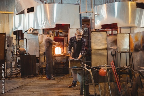 Team of glassblowers shaping a glass on the blowpipe photo