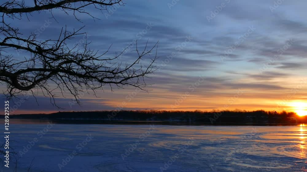 Panning across breathtaking frozen river at sunrise, from shore between gnarly old trees. Panning across breathtaking frozen river at sunrise, from shore between gnarly old trees.