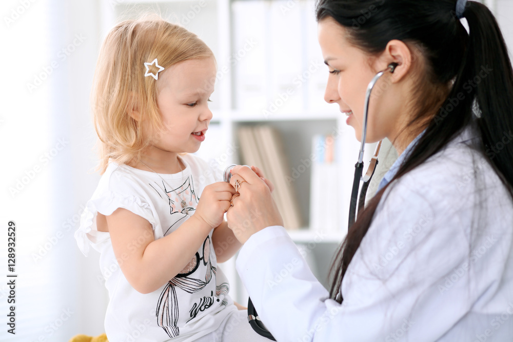 Pediatrician is taking care of baby in hospital. Little girl is being examine by doctor with stethoscope. Health care, insurance and help concept. Pediatrician is taking care of baby in hospital. Little girl is being examine by doctor with stethoscope. Health care, insurance and help concept.
