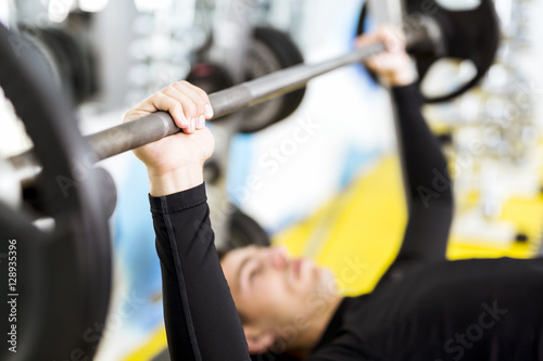 Closeup of young handsome man doing exercises on a bench press