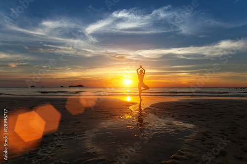 Small silhouette of a woman practicing yoga on sea beach during amazing sunset.