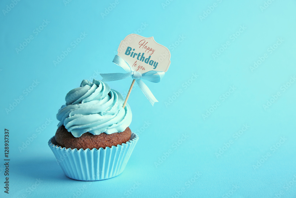 Delicious cupcake with greeting card on blue background. Text HAPPY