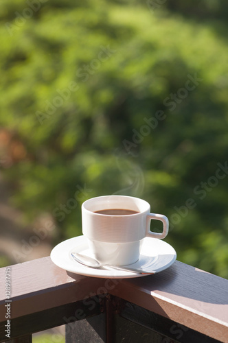 White cup of hot coffee on balcony with natural background.