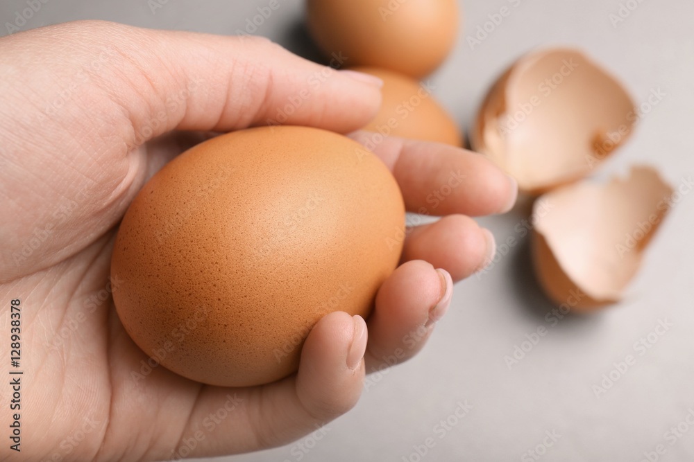 Female hand holding raw egg on light background Female hand holding raw egg on light background