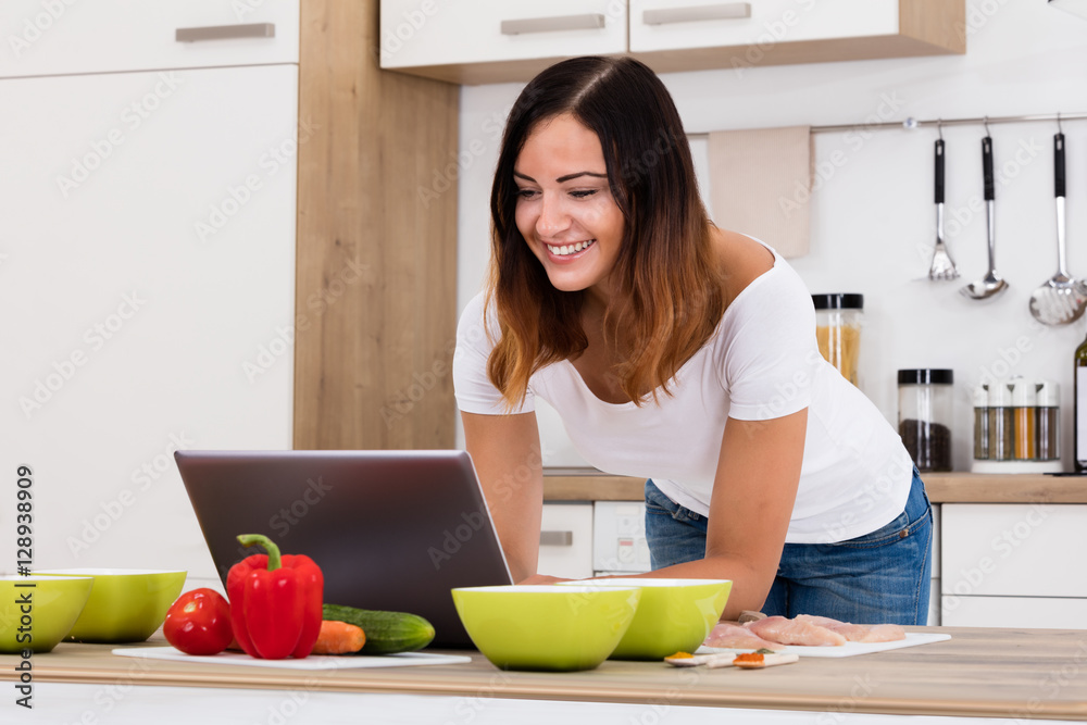 Smiling Woman Using Laptop In Kitchen Smiling Woman Using Laptop In Kitchen