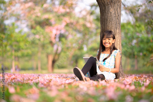 Obraz na płótnie Happy asian girl sitting on grass with tablet computer in the park w salonie