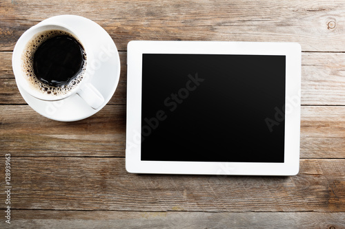 White tablet computer on a wooden table with cup of black coffee
