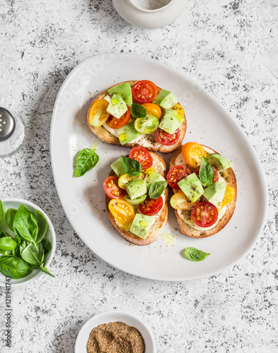 Cherry tomatoes, avocado and basil bruschetta. On a light background. Healthy snack or appetizer with wine