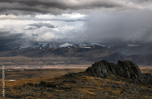 Rocks and valley of the mountain river on a background of high peaks covered with snow ranges under rain from the storm dramatic dark scary clouds Plateau Ukok Altai Siberia Russia