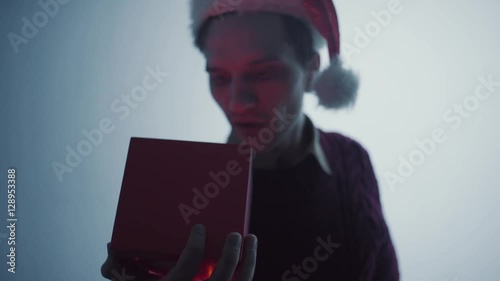 Young man in red Santa Claus hat openinng gift box surprised and happy with what you see photo