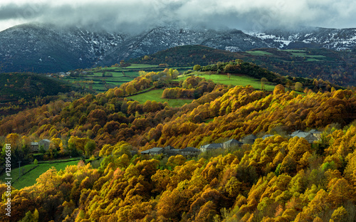 Montaña con algunas casa en medio en pleno otoño con los picos nevados generando un contraste interesante photo