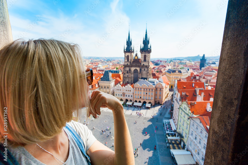Kostel Panny Marie pred Tynem. Church of the Virgin Mary. A young woman stands on top of the clock tower and looks at the Old Town Square in Prague - obrazy, fototapety, plakaty 